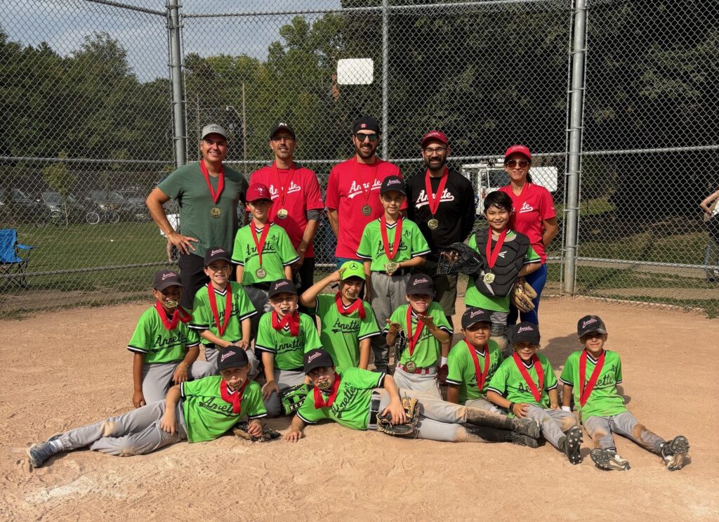 A photo of a youth baseball team celebrating with their championship medals, taken at home plate