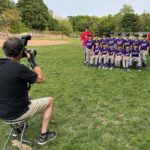 A photographer taking a team photo of a baseball team wearing purple on photo day
