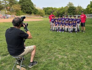 A photographer taking a team photo of a baseball team wearing purple on photo day